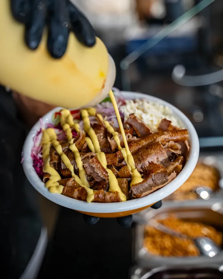 Doener-Bowl in der Hand, Kaesesauce wird darueber gegossen