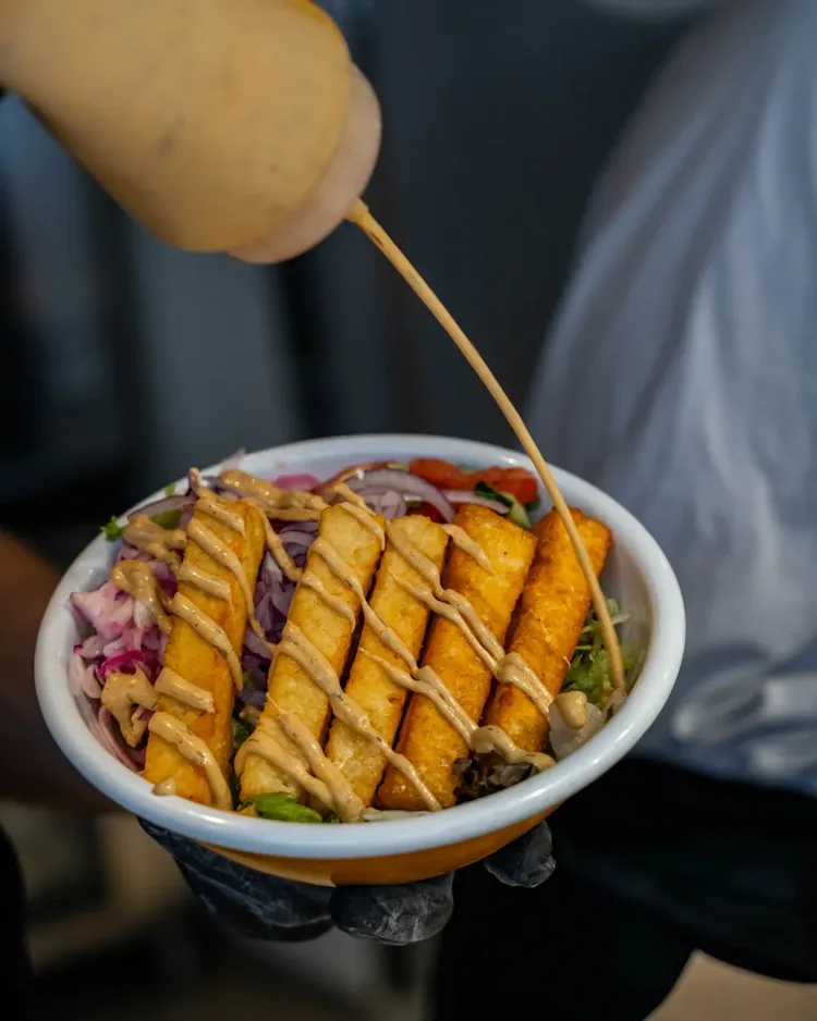 Halloumi-Bowl in der Hand, Sauce wird darueber gegossen
